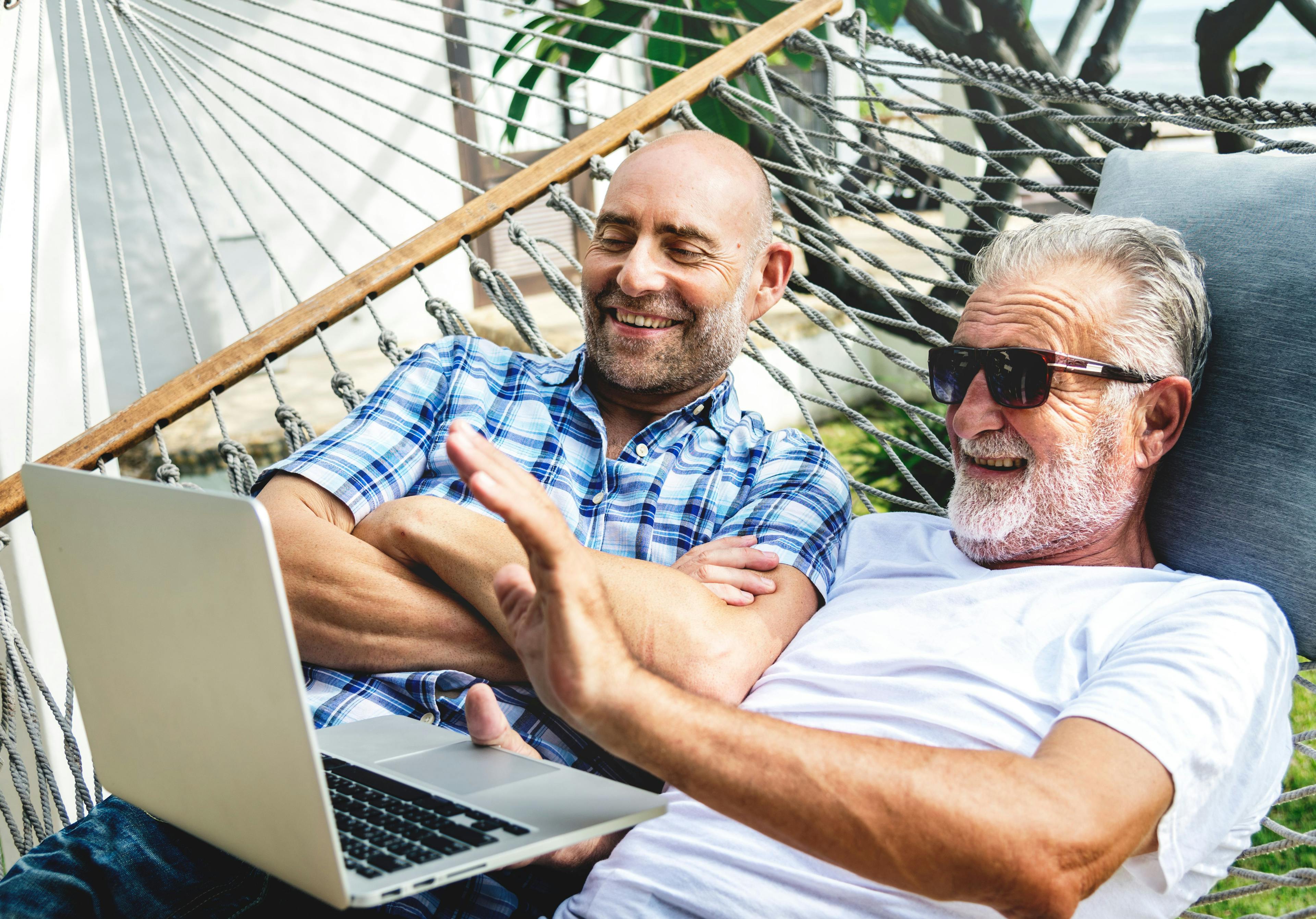 Zwei ältere Männer mit dem Laptop auf einer Hängematte.