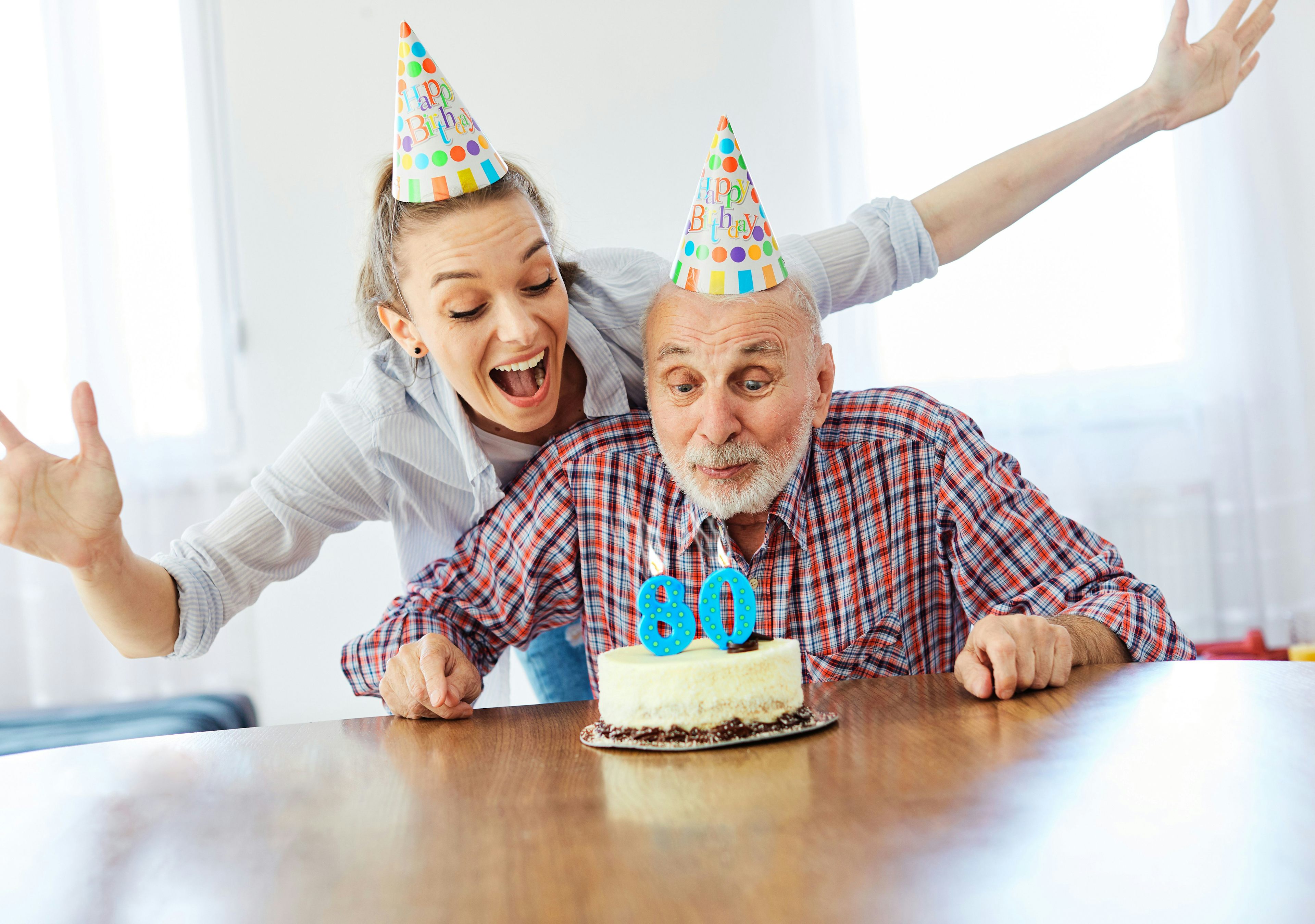 Ein Senior feiert seinen 80. Geburtstag mit einem Kuchen und einer jungen Frau.
